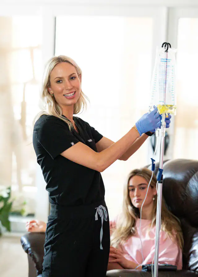 A Drip Lab nurse hangs an IV bag as a client rests in a recliner by the window