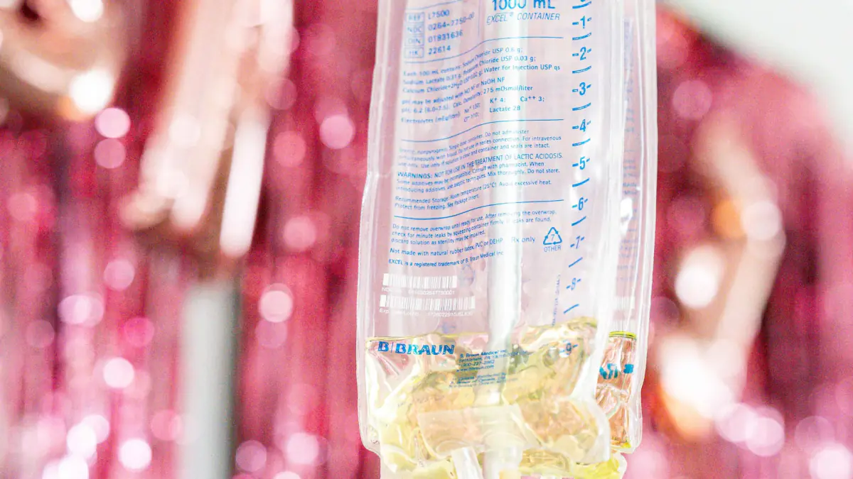 A one-liter bag of IV fluids hangs in front of pink tinsel and rose gold balloons