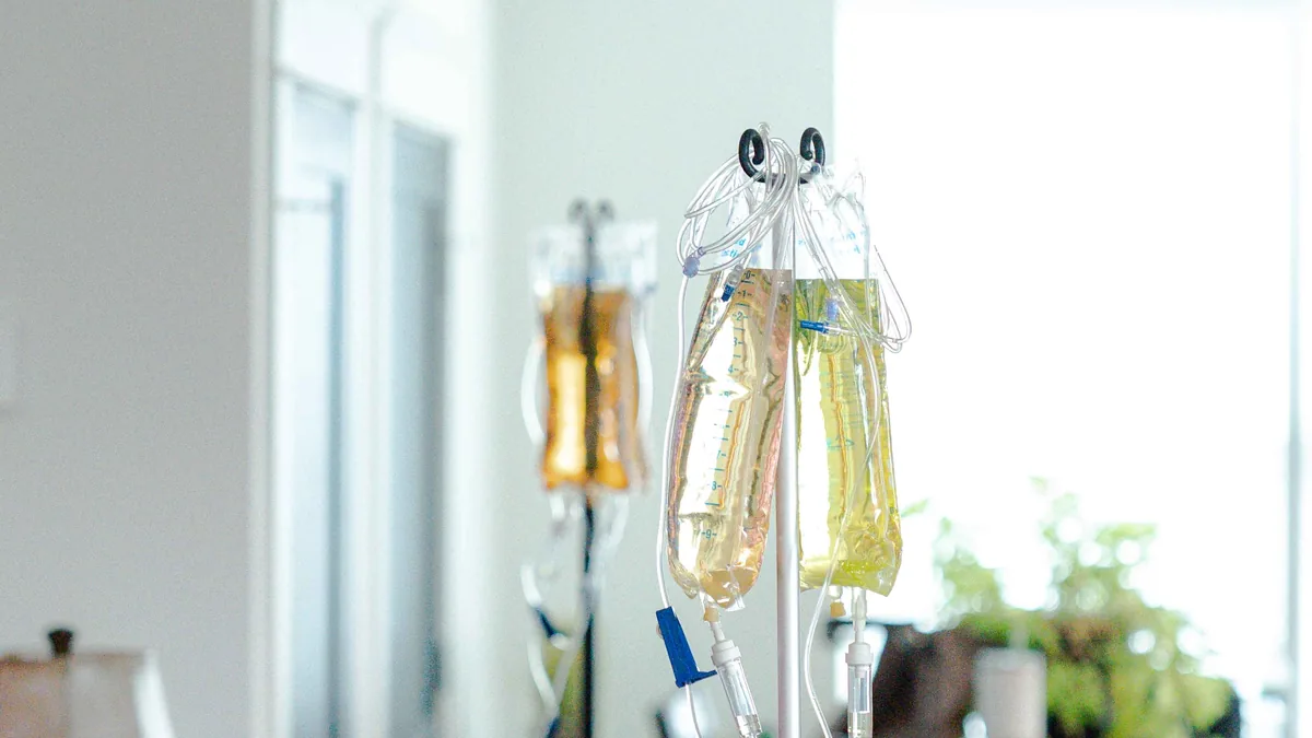 IV bags in amber and yellow hang from two IV stands in a bright living room